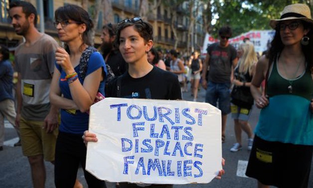 A protester carrying a placard reading "Tourist flats displace families" in Barcelona. Hordes of tourists in Europe have “evicted” residents - AFP