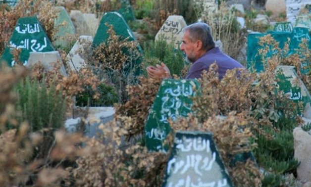 © AFP / by Omar Haj Kadour | A Syrian man prays in a cemetery in Khan Sheikhun, a rebel-held town in northwestern Syria, on July 12, 2017, 100 days after a sarin gas attack killed at least 87 people, including children
