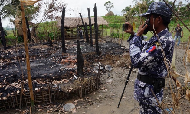 A Myanmar border guard police officer takes pictures at the remains of a burned house in Tin May village, northern Rakhine state - Reuters/Simon Lewis