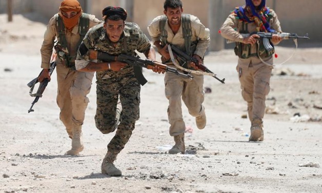 Kurdish fighters from the People's Protection Units run across a street in Raqqa, Syria. REUTERS