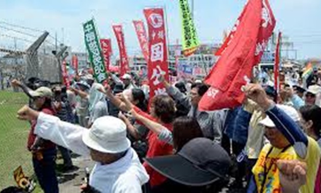 © JIJI PRESS/AFP/File | People raise their fists as they shout slogans to protest against the US military presence in front of the US Kadena Air Base in Cyatan, Okinawa prefecture in 2016
