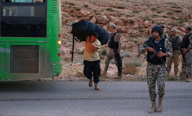 Lebanese policemen and Hezbollah fighters are seen as a Syrian man carries his bag near a bus in Jroud Arsal- Reuters