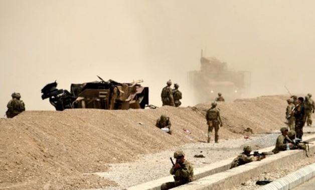 © AFP / by Thomas WATKINS | US soldiers keep watch near the wreckage of their vehicle at the site of a Taliban suicide attack in Kandahar on August 2, 2017