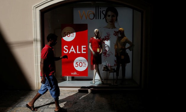 An African migrant walks past a Wallis clothing store shop window advertising a sale in Valletta - REUTERS