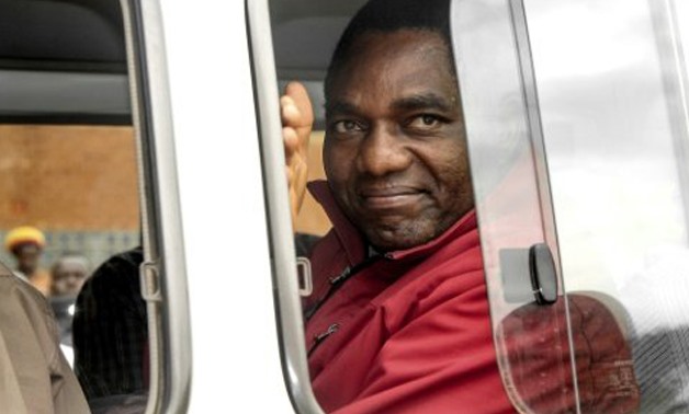 © AFP/File | Zambian opposition leader Hakainde Hichilema waves to supporters from a police van as he leaves a courtroom in April