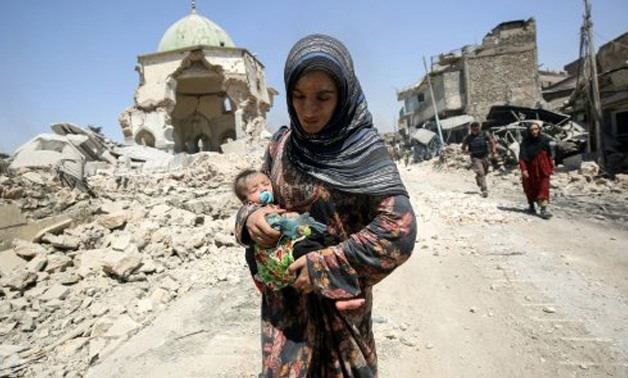 © AFP/File / by Sarah Benhaida | An Iraqi woman carrying a child walks by the destroyed Al-Nuri Mosque as she flees the Old City of Mosul on July 5, 2017