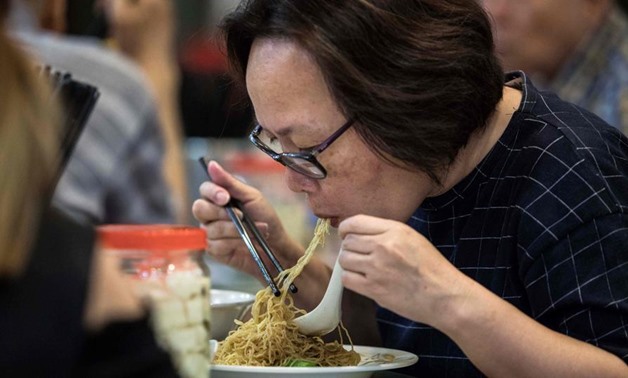 A woman eats noodles, handmade using a traditional bamboo pole technique, at a restaurant in Hong Kong -
 AFP