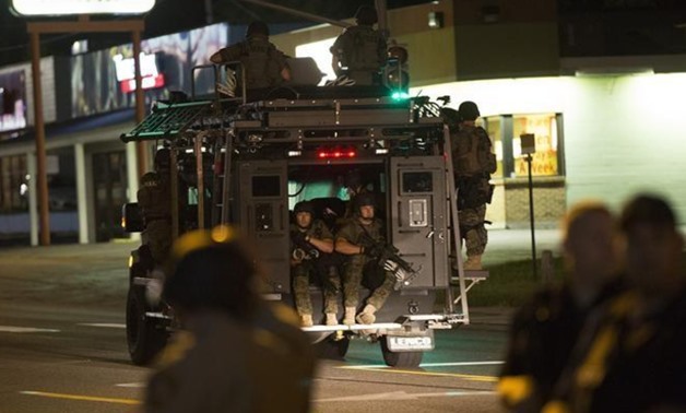 Police officers ride an armored vehicle as they patrol a street in Ferguson