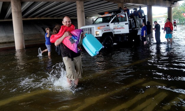 A man carries a child after being evacuated by dump truck from the Hurricane Harvey floodwaters in Dickinson, Texas August 28, 2017. — Reuters pic