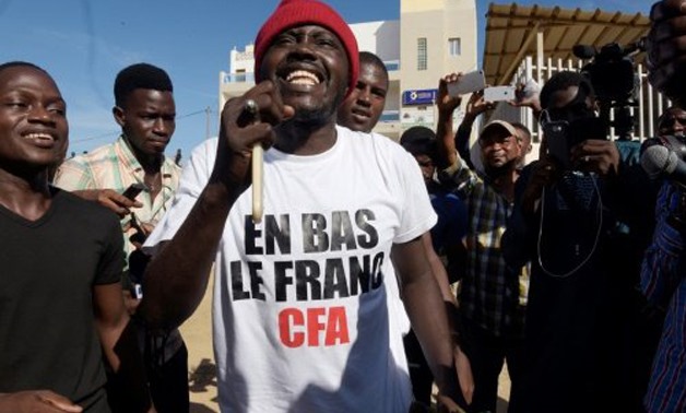 AFP | Supporters of controversial activist Kemi Seba celebrate his acquital on charges of burning a CFA banknote outside a court in Senegal's capital Dakar, one wearing a t-shirt reading: 'Down with the CFA franc'