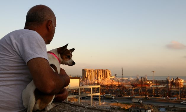 Michel Assad with his dog Pepsi look at the damaged site of Tuesday's blast in Beirut's port area from the roof of his home in Beirut, Lebanon, August 7, 2020. REUTERS/Hannah McKay
