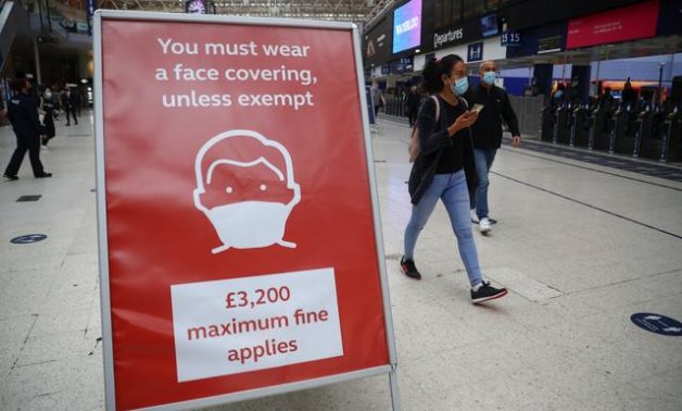 People wearing protective face masks pass a sign at Waterloo station during the morning rush hour, amid the coronavirus disease (COVID-19) outbreak, in London, Britain, September 23, 2020. REUTERS/Hannah McKay