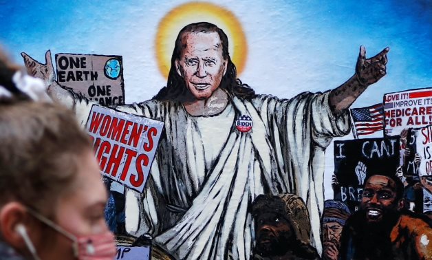 A woman walks past a mural depicting U.S. President Joe Biden as Jesus addressing crowds of people titled 'The Saviour', created by artist Harry Greb in Rome, Italy, January 21, 2021. REUTERS/Yara Nardi