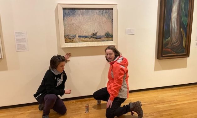 This photo provided to media from the group Stop Fracking Around shows Erin Fletcher, left, and Emily Kelsall, right, in front of the Emily Carr painting, Stumps and Sky, at the Vancouver Art Gallery 