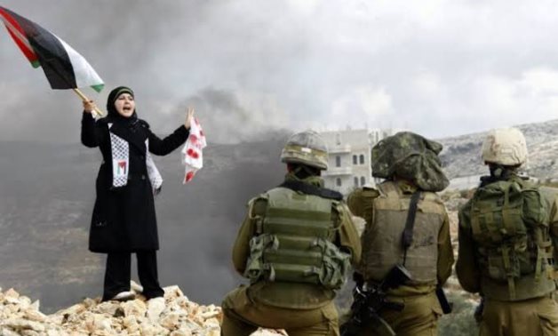 Palestinian woman raises the Palestinian flag and stands defiant against Israeli soldiers- photo taken from Abu Zeid’s X account