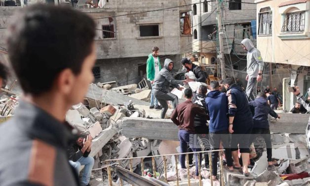A Palestinian child observes as a group of people moves a wrapped body of a deceased person amidst the rubble of a building destroyed by Israeli bombings - WAFA