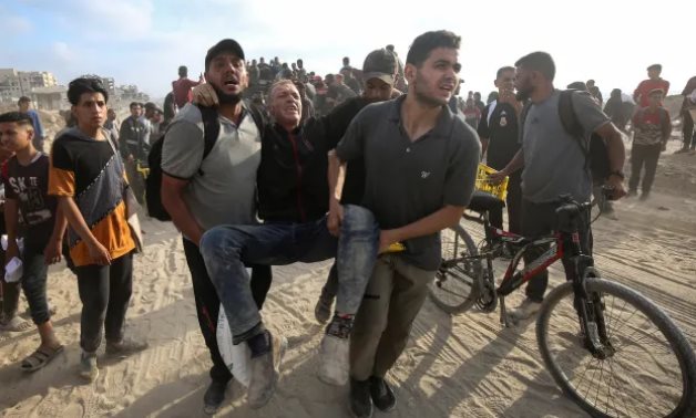 Two young Palestinians in Gaza carry an injured man as Israeli troops continue to shoot at civilians during the 20-month war in the enclave - Photo by WAFA