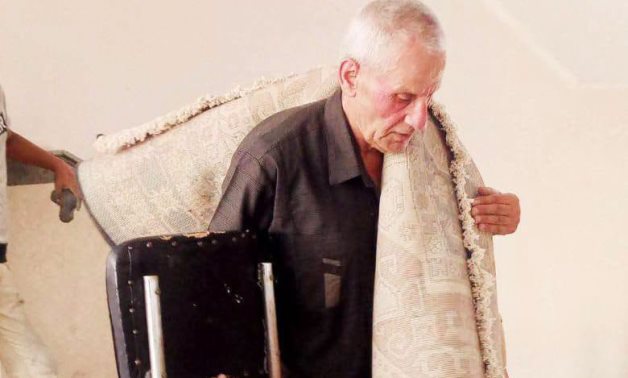 Professor Emeritus Habib Abu Jumaa carrying a rug over his shoulder and a chair in his hand while assisting with the move to the college's new building