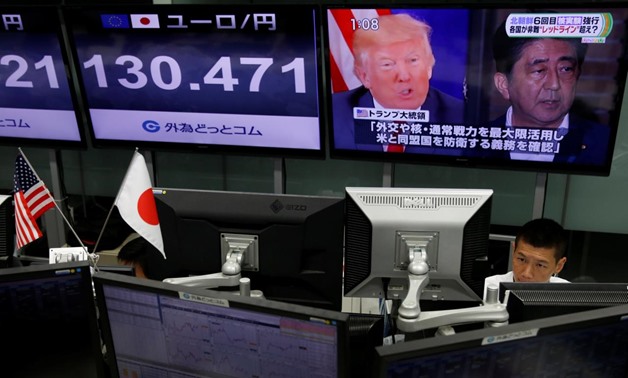 An employee of a foreign exchange trading company works near a monitor showing Japan's Prime Minister Shinzo Abe and U.S. President Donald Trump in a television news report about their telephone conference on North Korea's threat in Tokyo, Japan September