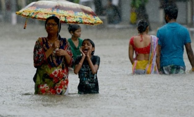 © AFP/File / by Vishal MANVE | Indian people are seen wading through a flooded street last month during heavy rain showers in Mumbai