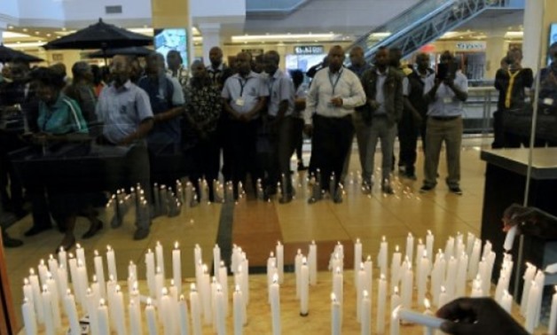 © AFP/File / by Tristan MCCONNELL | Staff of the Nakumatt supermarket chain gather in front of candles lit to mark the second anniversary commemorations of the Westgate shopping mall attack by militants