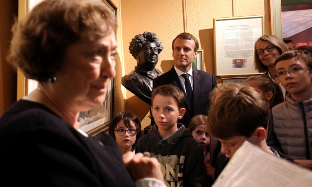 French President Emmanuel Macron (C Rear) stands next to a bust of author Alexandre Dumas as he looks on with schoolchildren and French Minister of Culture Francoise Nyssen (2ndR) as a guide speaks during a visit to the Chateau de Monte-Cristo at Marly-le