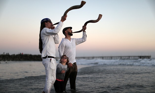 Jared Stein (L) and Daniel Levitch (R) blow the shofar as Gillian Levitch, 4, watches at a Tashlich ceremony, a Rosh Hashanah ritual to symbolically cast away sins, during the Nashuva Spiritual Community Jewish New Year celebration on Venice Beach in Los 
