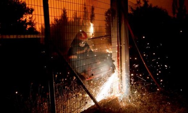 A firefighter cuts a metal fence as a wildfire burns near the village of Metochi, north of Athens, Greece, August 15, 2017.... Giorgos Moutafis August 16, 2017 01:19pm BST