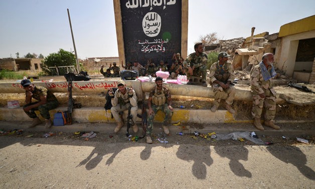 Shi'ite Popular Mobilization Forces (PMF) sit next to the black flag sign commonly used by Islamic State militants, after liberating the city Hawija - REUTERS