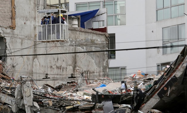 People stand in a personnel crane basket while looking at the remains of a building that collapsed in the earthquake - REUTERS