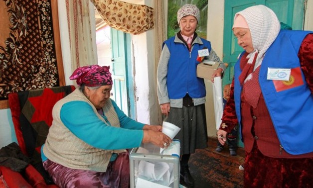A woman casts her ballot next to visiting members of a local electoral commission during early voting at the presidential election in the village of Arashan outside Bishkek, Kyrgyzstan October 14, 2017. Photo: Reuters