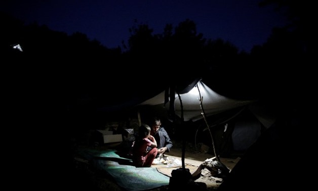 A father and his children eat under a tent at a makeshift camp on the Greek island of Samos - REUTERS