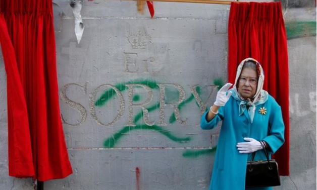 A person, dressed as Britain's Queen Elizabeth II, gestures during an event ahead of the anniversary of the Balfour Declaration, outside Banksy’s Walled Off Hotel in the West Bank city of Bethlehem November 1, 2017 -
 REUTERS/Mussa Qawasma/File Photo