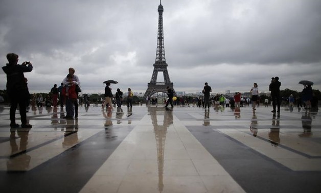 Tourists stroll on the Trocadero square, in front of the Eiffel Tower during a rainy summer day in Paris, August 7, 2013. REUTERS/Christian Hartmann