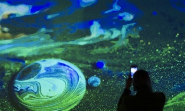 © AFP / by Olivia HAMPTON | A woman takes a photo of the Kingdom of Colors exhibition, an immersive visual experience from French filmmaker Thomas Blanchard and artist Oilhack in Washington DC