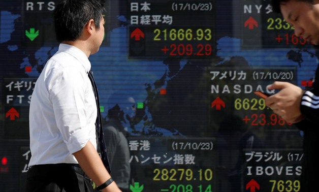 Passersby walk past an electronic board showing market indices outside a brokerage in Tokyo, Japan, October 23, 2017. REUTERS/Issei Kato