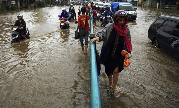 A woman holds a street divider as she walks through a flooded street in Jakarta, January 24, 2014 - Reuters 