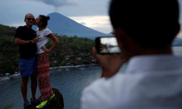 Tourists from Russia pose while having their photograph taken with Mount Agung volcano erupting in the background from Amed, Karangasem Regency, Bali, Indonesia, November 30, 2017. REUTERS/Darren Whiteside
