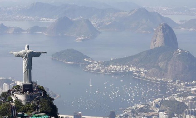 Tourists visit the Christ the Redeemer statue with Sugarloaf Mountain (R) in the distance in Rio de Janeiro/ REUTERS