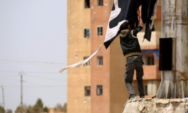 © AFP / by Rouba El Husseini | A member of the US-backed Syrian Democratic Forces (SDF) removes an Islamic State group flag in the northern town of Tabqa on April 30, 2017 after capturing it from the jihadists
