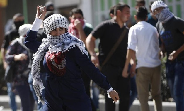 A Palestinian woman hurls stones at Israeli troops during clashes in the West Bank city of Hebron October 13, 2015. REUTERS/Mussa Qawasma