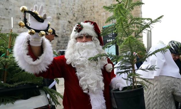 Israeli-Arab Issa Kassissieh, wearing a Santa Claus costume, holds a small tree and a bell during the annual Christmas tree distribution by the Jerusalem municipality in Jerusalem's Old City December 21, 2017. REUTERS/Ammar Awad