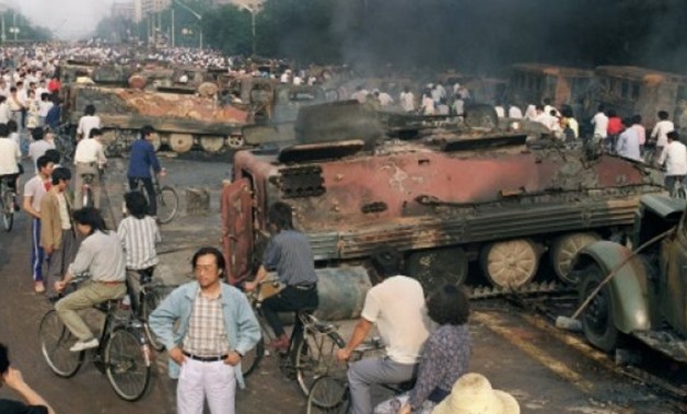 Beijing residents gather around the smoking remains of over 20 armoured personnel carriers burnt by demonstrators during clashes with soldiers near Tiananmen Square on June 4, 1989 - AFP/File 