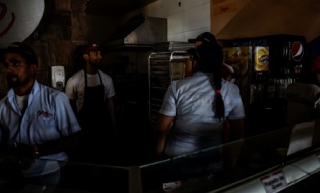 Employees stand inside a fast food shop during a power cut in Caracas, the capital of crisis-hit Venezuela, which saw its economy shrink by a massive 16.5 percent in 2016 - AFP