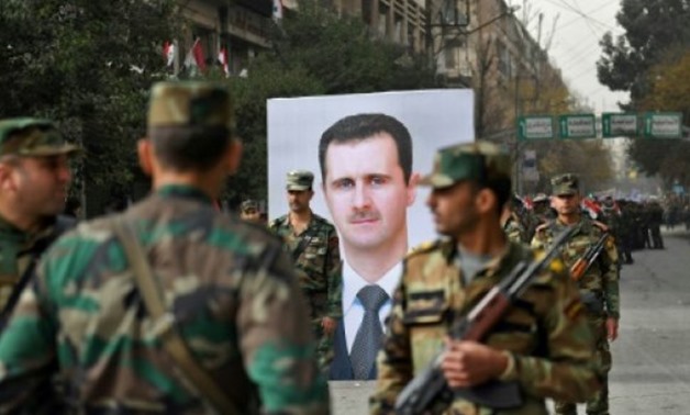 © AFP | Syrian soldiers walk past a portrait of President Bashar al-Assad during a government celebration marking the first anniversary of the retaking of the northern Syrian city of Aleppo
