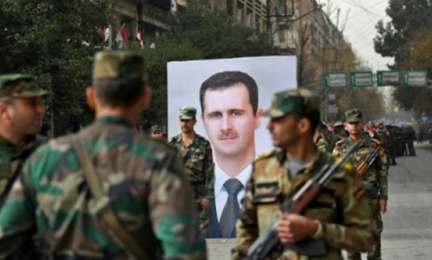 © AFP | Syrian soldiers walk past a portrait of President Bashar al-Assad during a government celebration marking the first anniversary of the retaking of the northern Syrian city of Aleppo
