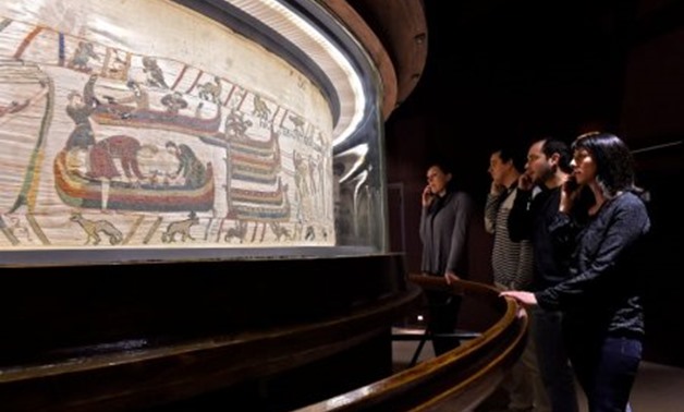 People stand in front of the Bayeux Tapestry, an 11th century treasure that tells the tale of how William the Conqueror came to invade England in 1066, in this undated photo provided by the Bayeux Museum in France, on January 18, 2018. Bayeux Museum/Steph