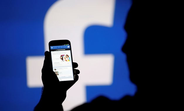 A man is silhouetted against a video screen with an Facebook logo as he poses with an Samsung S4 smartphone in this photo illustration August 14, 2013. REUTERS/Dado Ruvic/File Photo