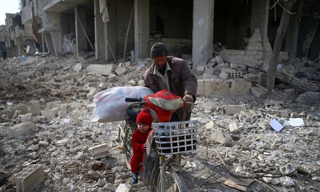 FILE PHOTO - A man is seen with a child who rides a bicycle inside damaged area in Misraba, Eastern Ghouta, near Damascus, Syria January 11, 2018 -
 REUTERS/Bassam Khabieh