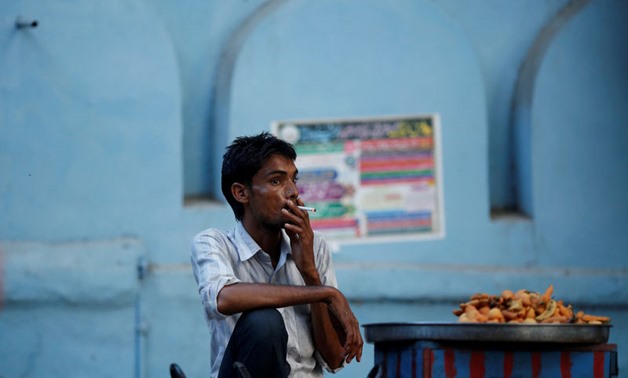 FILE PHOTO: A snack vendor smokes a cigarette as he waits for customers on a street in New Delhi - Reuters
